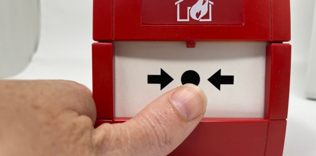 fire alarm call point with mans thumb pointing at it