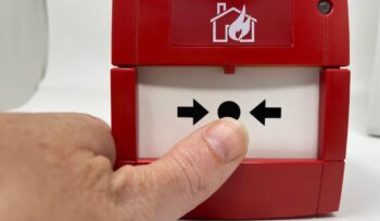 fire alarm call point with mans thumb pointing at it